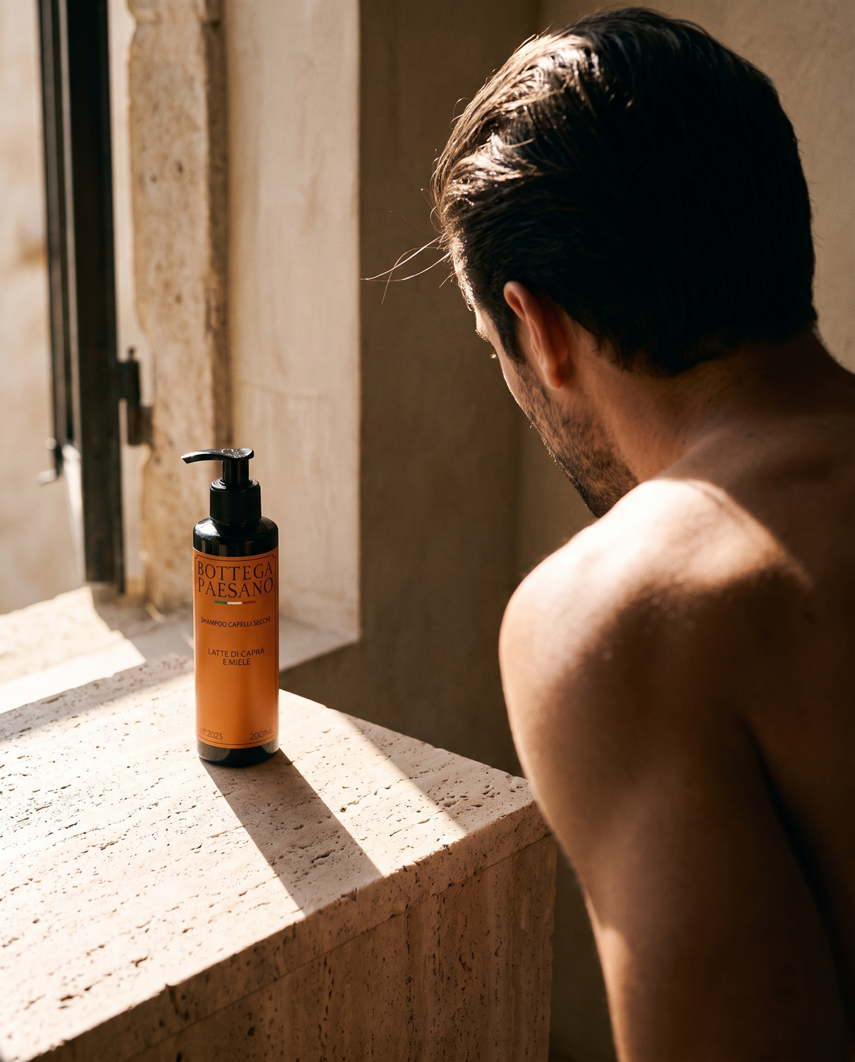 Uomo alla finestra con capelli fini, shampoo volumizzante Bottega Paesano sul davanzale